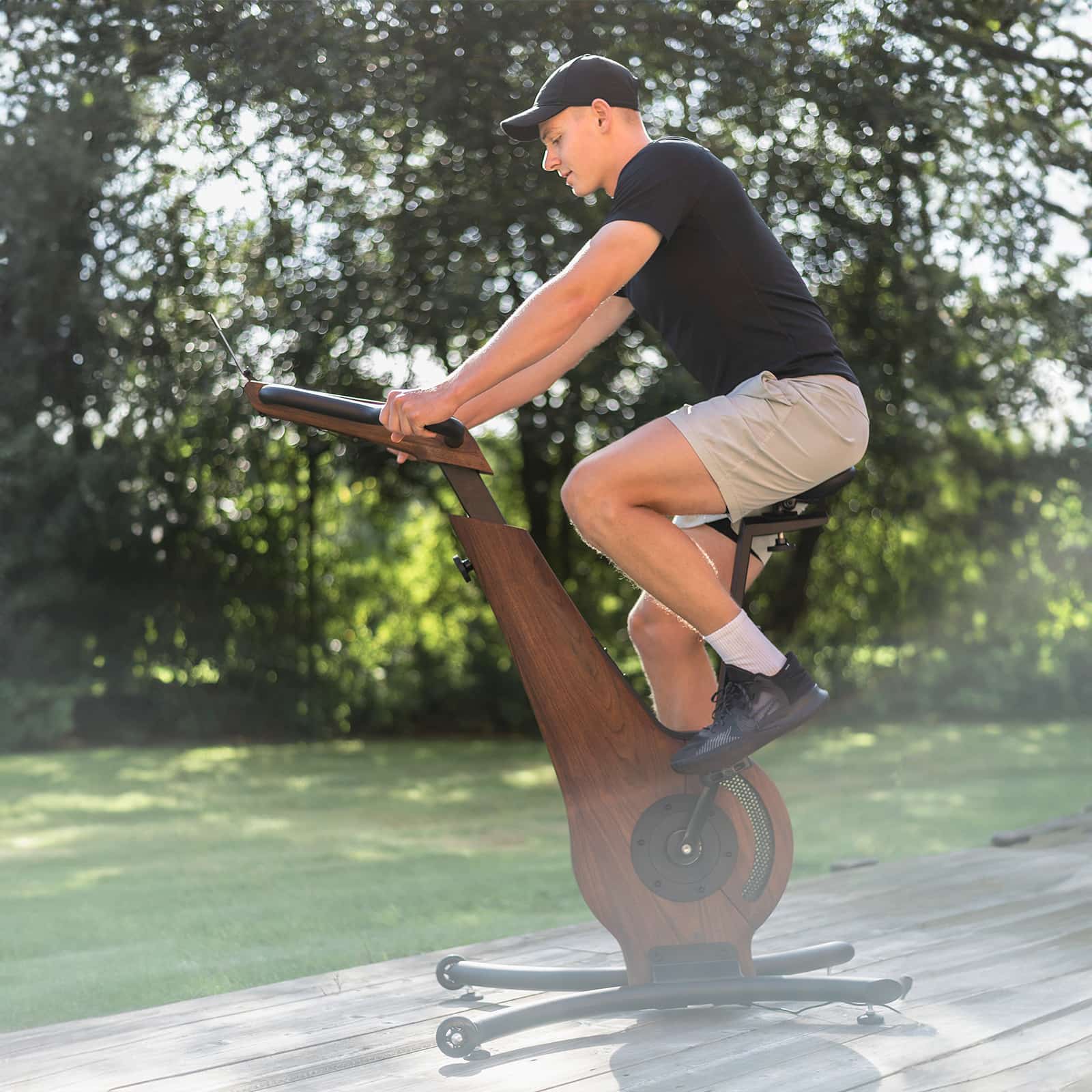 Ein Mann trainiert auf dem NOHRD Bike aus Walnussholz im Freien auf einer Holzterrasse.