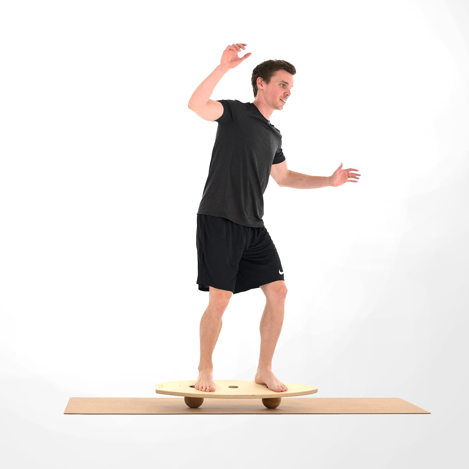 Ein Mann in schwarzer Sportkleidung trainiert barfuß sein Gleichgewicht im aufrechten Stand auf einem großen rollholz Balanceboard, das stabilisierend auf zwei Holzkugeln gelagert ist.
