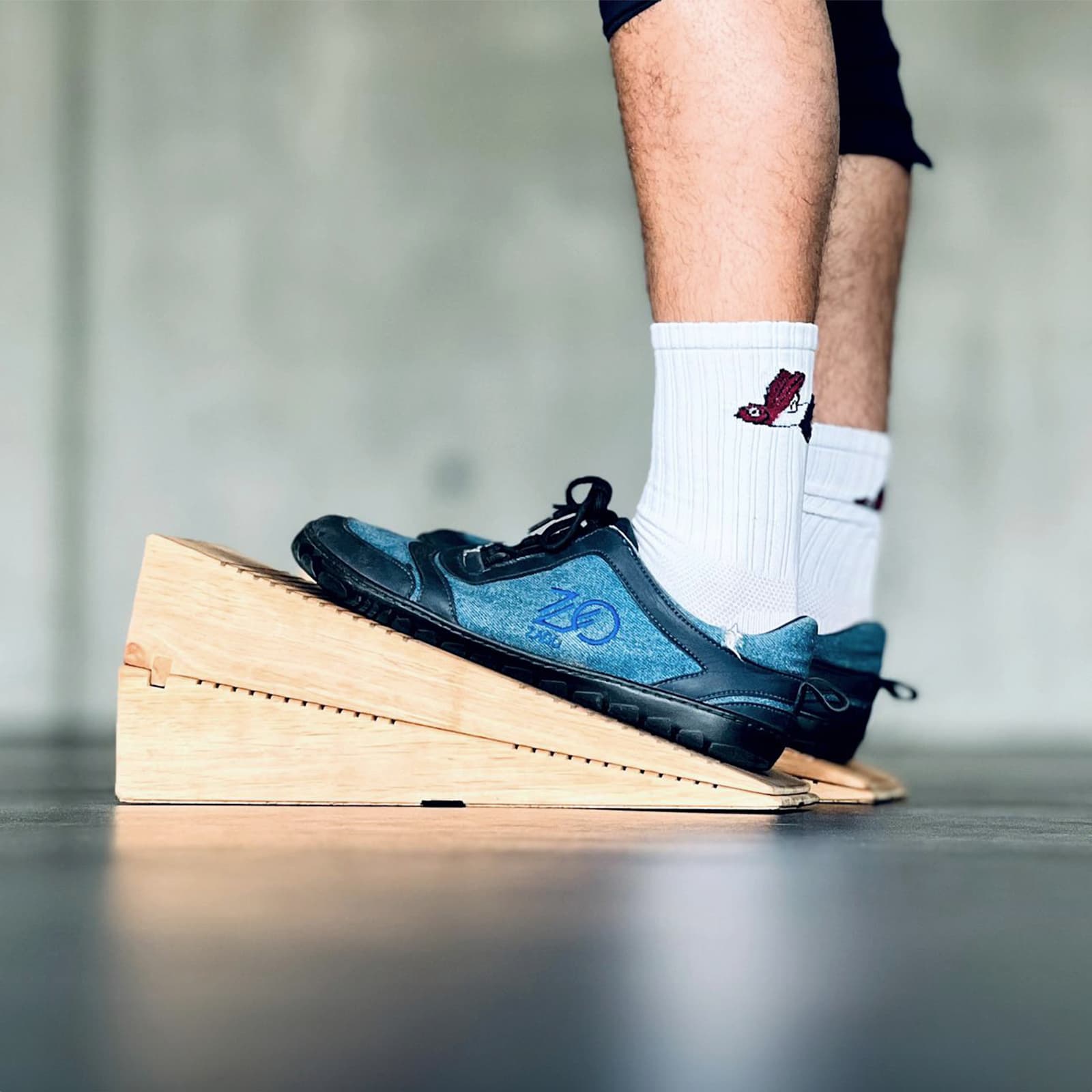 Nahaufnahme einer Person in Sportschuhen, die auf den rollholz Dehnkeilen aus Holz steht, um die Wadenmuskulatur und Achillessehne im Studio intensiv zu dehnen.