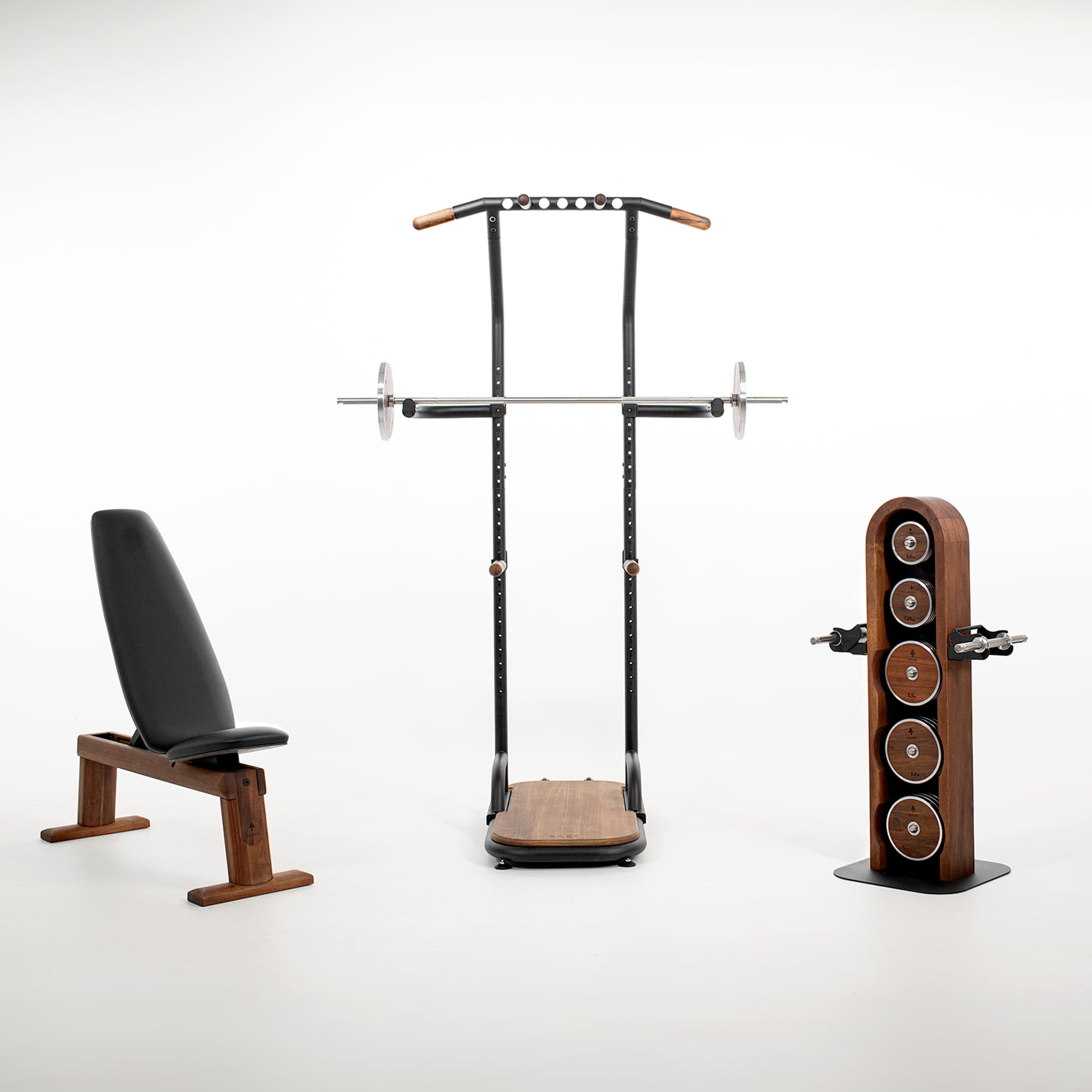 Ein hochwertiges Home-Gym-Set von NOHRD aus Walnussholz, bestehend aus der WeightBench Hantelbank, dem Squat Rack (BASE von rollholz) inklusive Langhantel und dem WeightPlate Tower, freigestellt auf weißem Hintergrund.