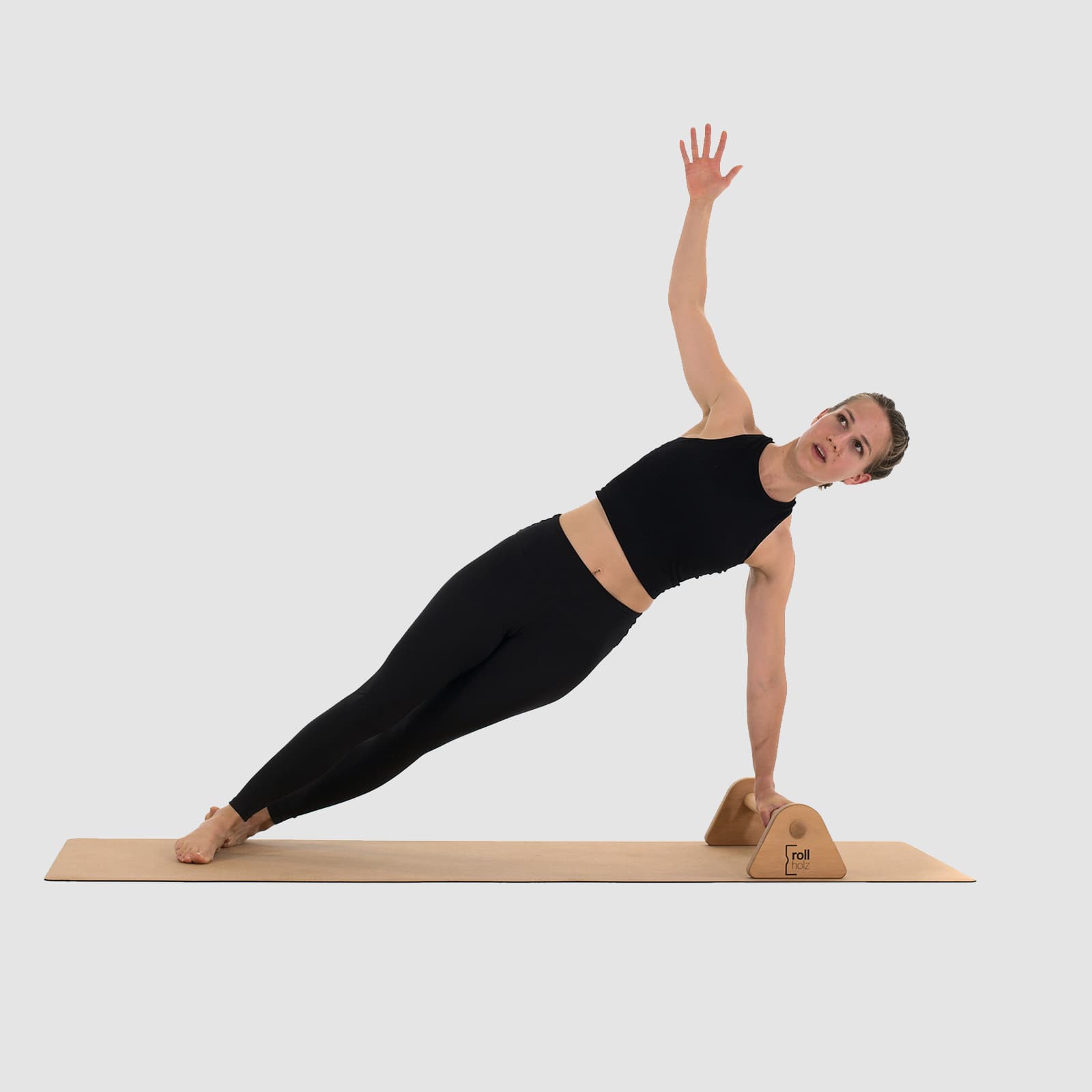 Eine Athletin in schwarzer Sportkleidung führt auf einer Korkmatte einen gestreckten Seitstütz (Side Plank) aus, während sie sich mit einer Hand an den rollholz Minibarren aus hellem Holz abstützt.