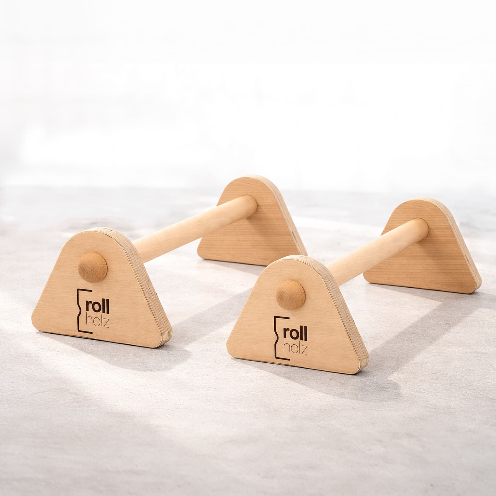 Ein Paar rollholz Minibarren aus hellem Echtholz mit eingebranntem Markenlogo, freigestellt in einer hellen Studio-Umgebung mit weichem Schattenwurf.
