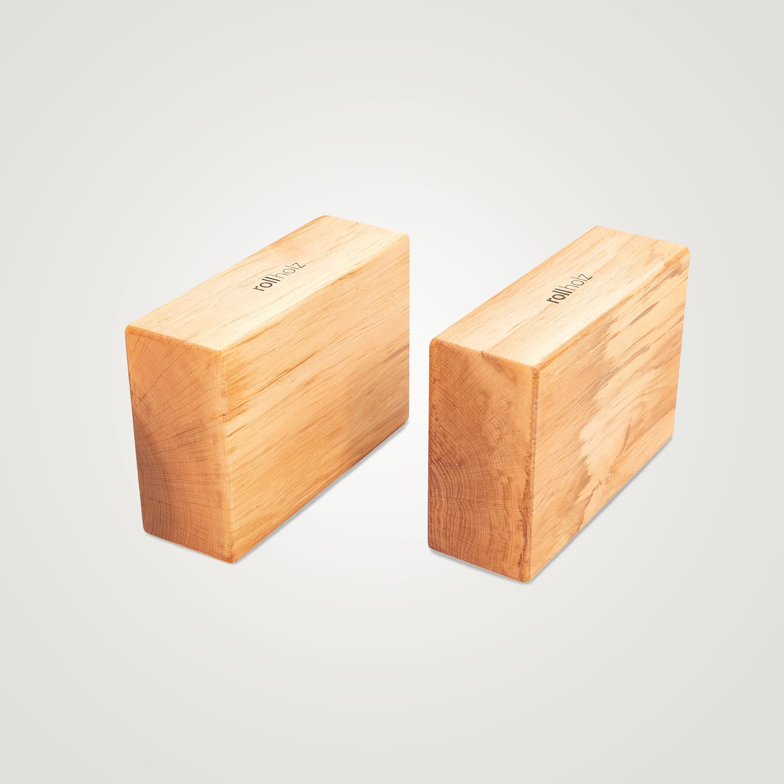 Zwei minimalistische rollholz Yoga-Blöcke aus warm gemasertem Erlenholz mit eingraviertem Markenlogo, nebeneinander platziert auf einem hellen Studio-Hintergrund.