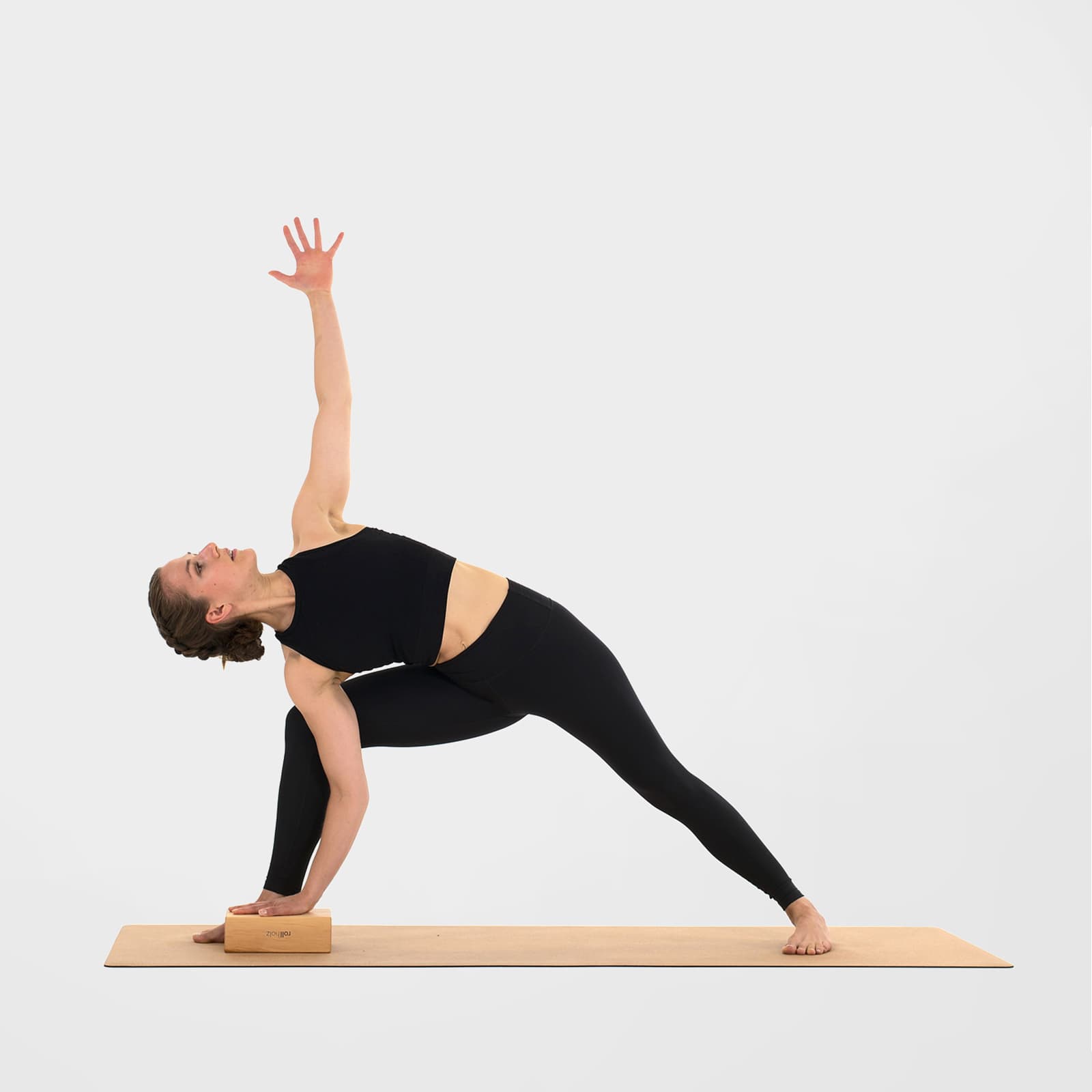 Eine Frau praktiziert den gestreckten seitlichen Winkel auf einer Korkmatte und nutzt einen rollholz Yogablock aus Erlenholz als stabile Erhöhung für die Hand.