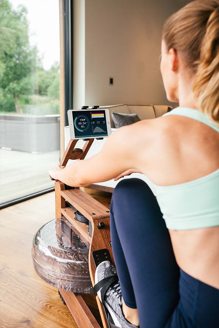 Frau trainiert am WaterRower Rudergerät aus Holz und verfolgt ihre Trainingswerte über die Tablet-App.
