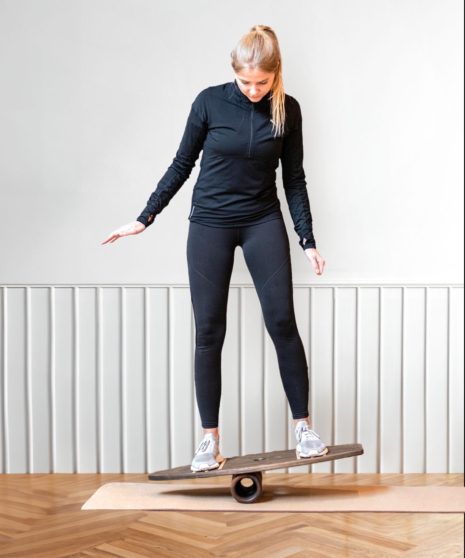 Frau beim Balancetraining auf einem Balance Board aus Holz im Innenbereich.
