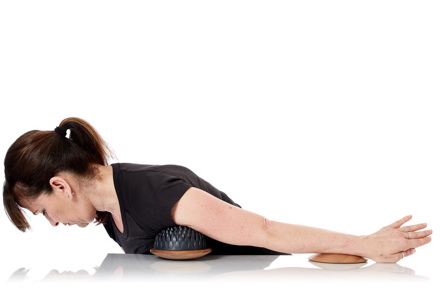 Femme allongée sur le ventre qui travaille le muscle pectoral avec un grand dôme Lotus sur base en bois