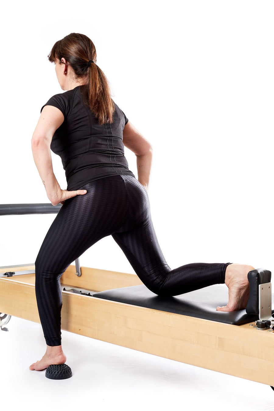 Femme en fente sur un reformer de Pilates, pied arrière sur un dôme Lotus, élévation du talon
