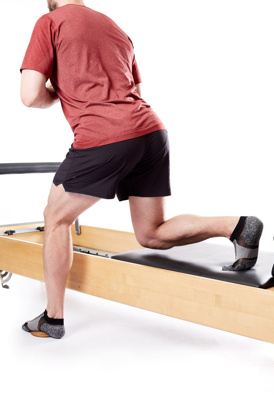 Homme en fente sur un reformer de Pilates, voûte plantaire activée sur une base en bois Lotus