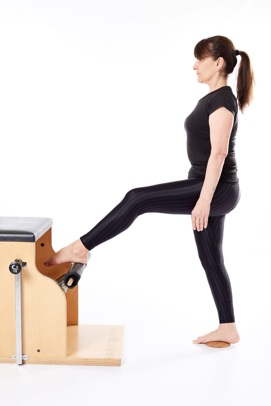 Femme debout sur une base en bois Lotus à côté du Wunda Chair, l'autre jambe levée sur la pédale
