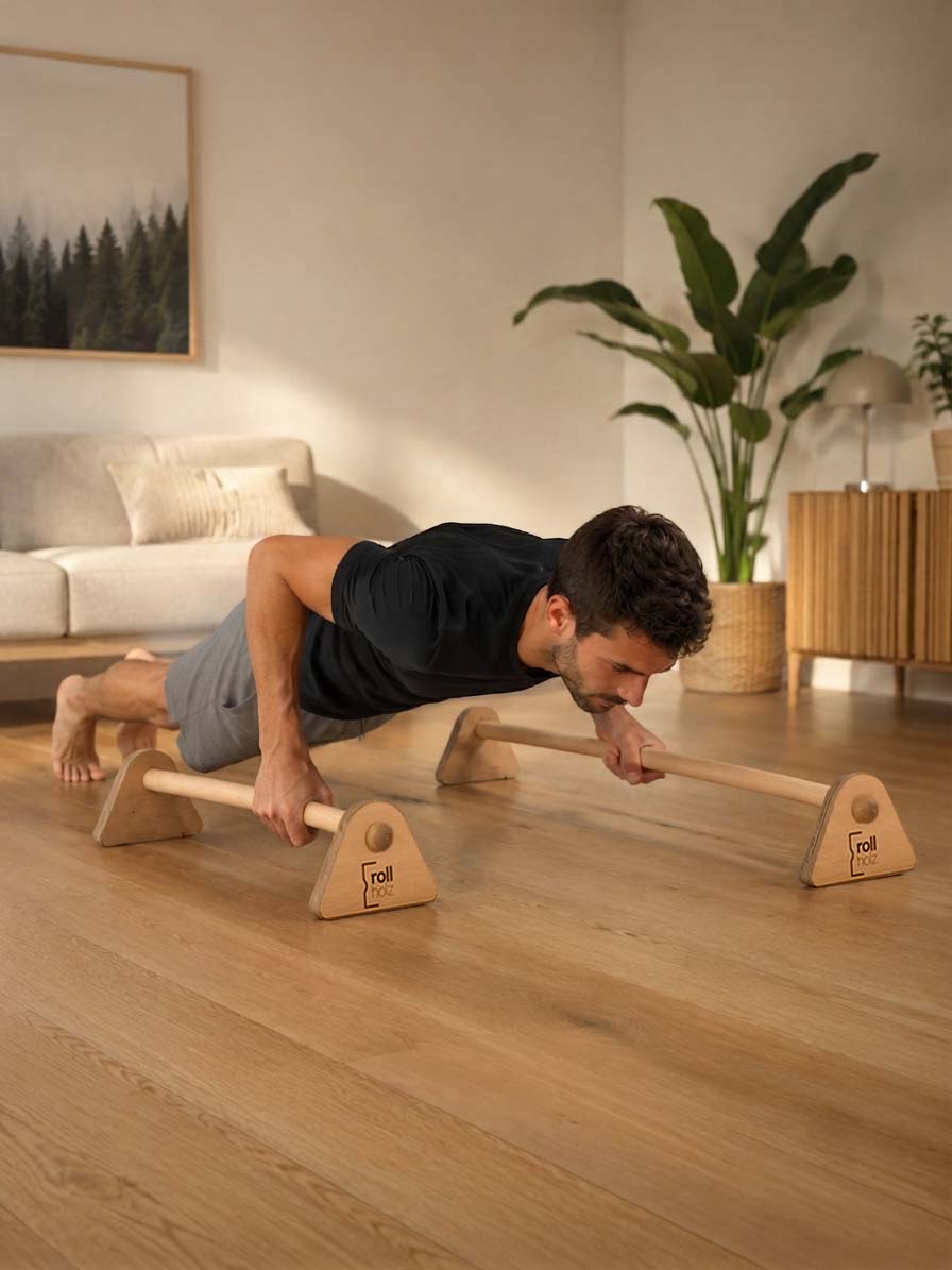 Holz-Parallettes für Liegestütze und Bodyweight-Training. Ein Mann trainiert mit zwei unterschiedlich langen Parallettes und führt tiefe Liegestütze in einem modernen Wohnraum aus.