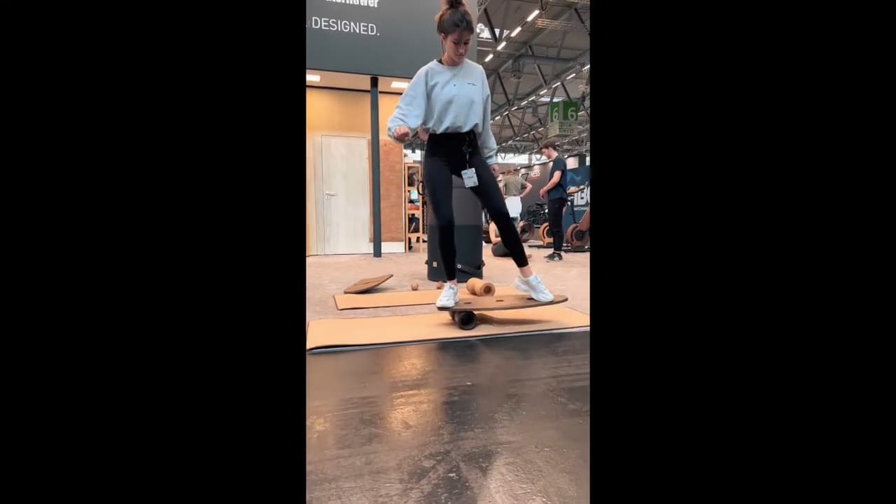 Eine junge Frau demonstriert das Gleichgewichtstraining auf einem rollholz Balance Board während einer Fitnessmesse.