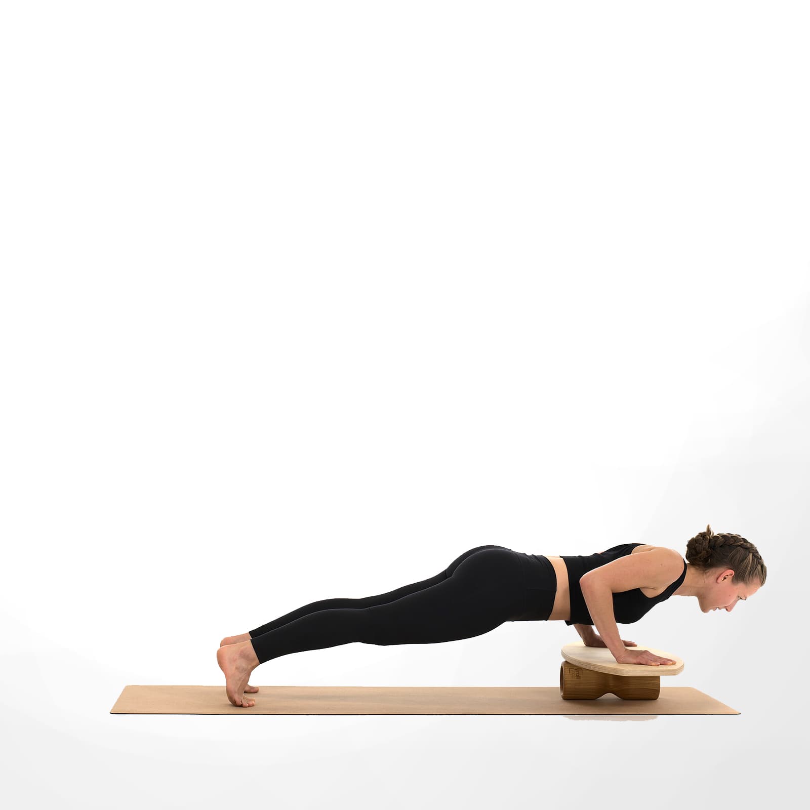 Eine Frau in schwarzer Sportkleidung führt auf einer Korkmatte Liegestütze (Push-Ups) aus, während ihre Hände auf dem instabilen rollholz Balanceboard balancieren.