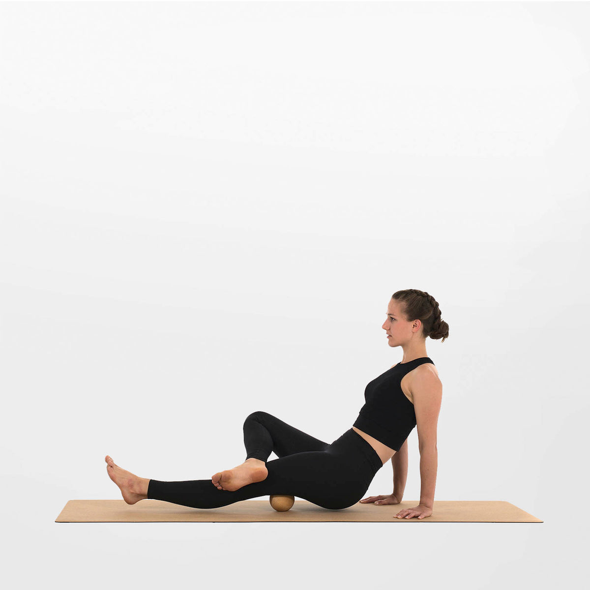 Femme utilisant une balle de massage en bois de 10 cm pour masser la cuisse et la zone fessière sur un tapis.