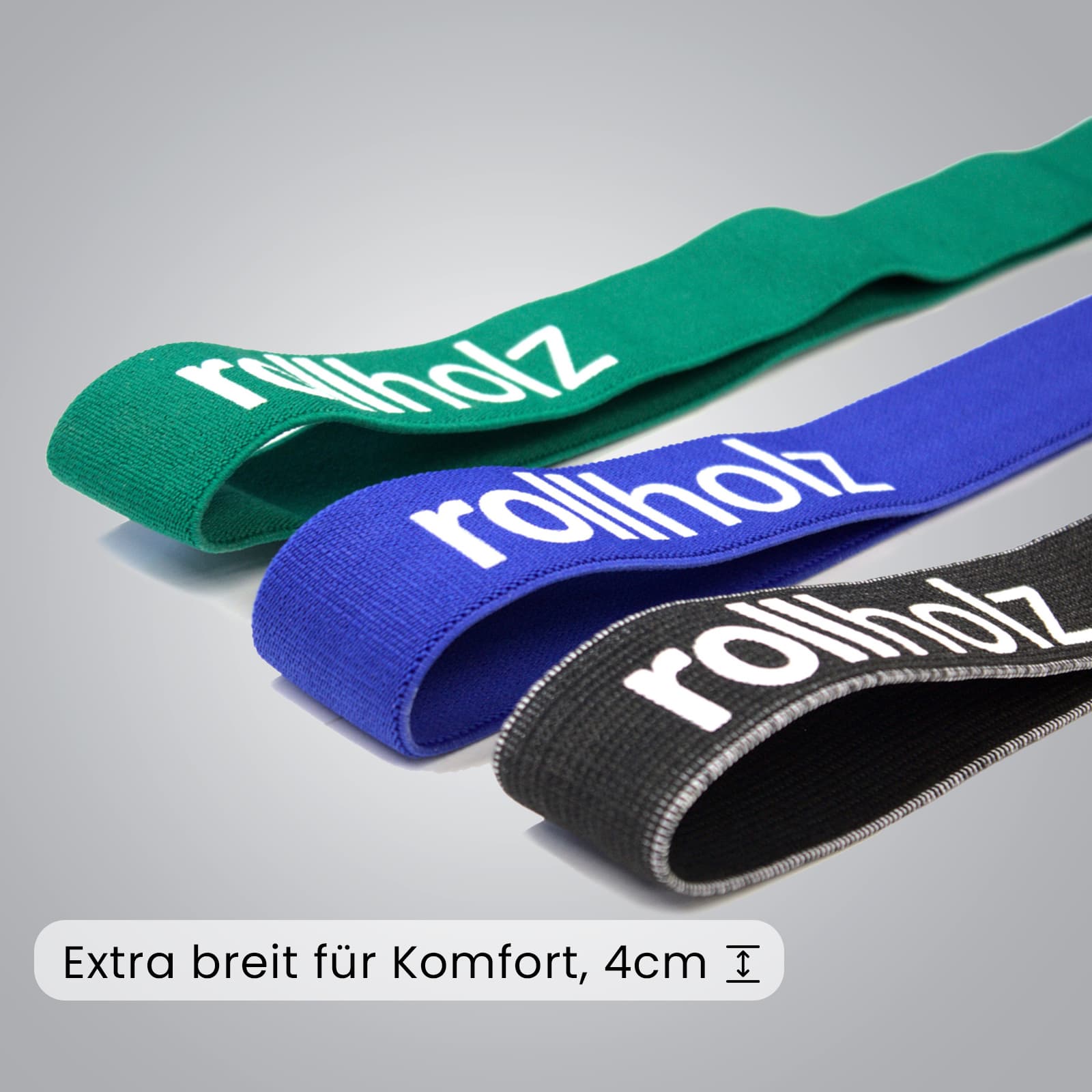 Nahaufnahme des rollholz Fitnessbänder-Sets mit Fokus auf die textile Struktur und die komfortable Breite von 4cm der grünen, blauen und schwarzen Bänder auf grauem Hintergrund.