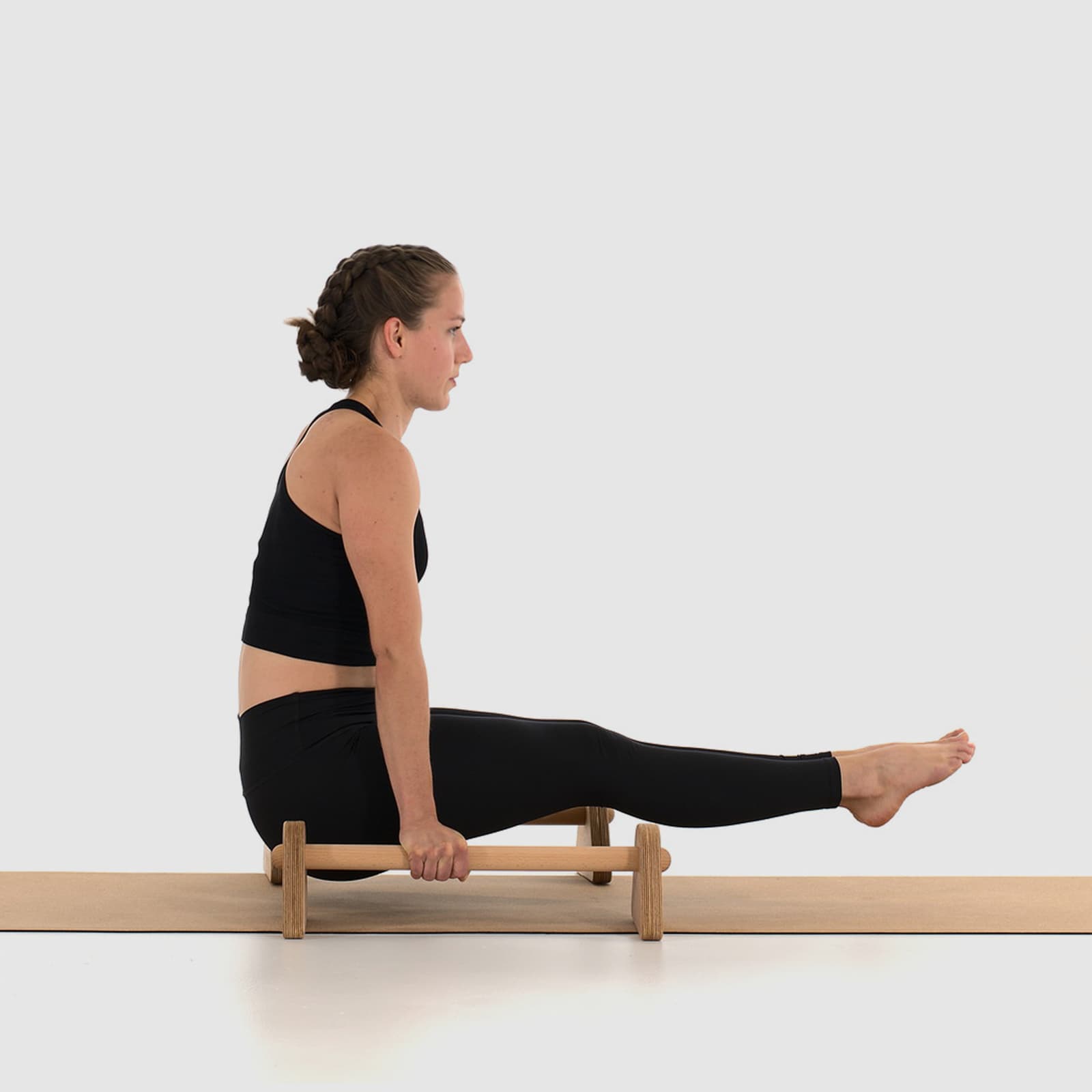 Eine Athletin in schwarzer Sportkleidung führt barfuß einen perfekten L-Sit (Haltetraining) auf den rollholz Minibarren aus Holz aus, die stabil auf einer Korkmatte platziert sind.