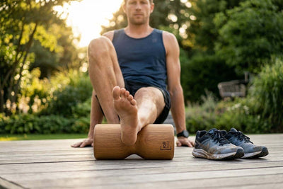 Läufer regeneriert nach dem Training auf einer Holzterrasse im Garten und rollt seine Wadenmuskulatur gezielt mit der rollholz Pro Faszienrolle im warmen Abendlicht aus.