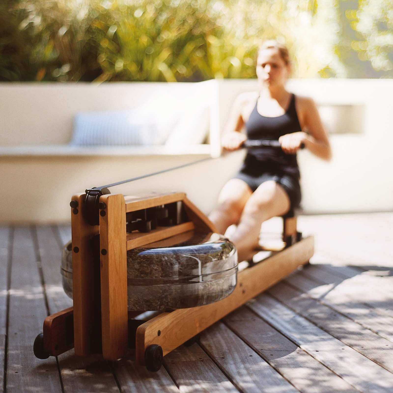 Frau trainiert auf einer Terrasse mit einem WaterRower Rudergerät aus Holz