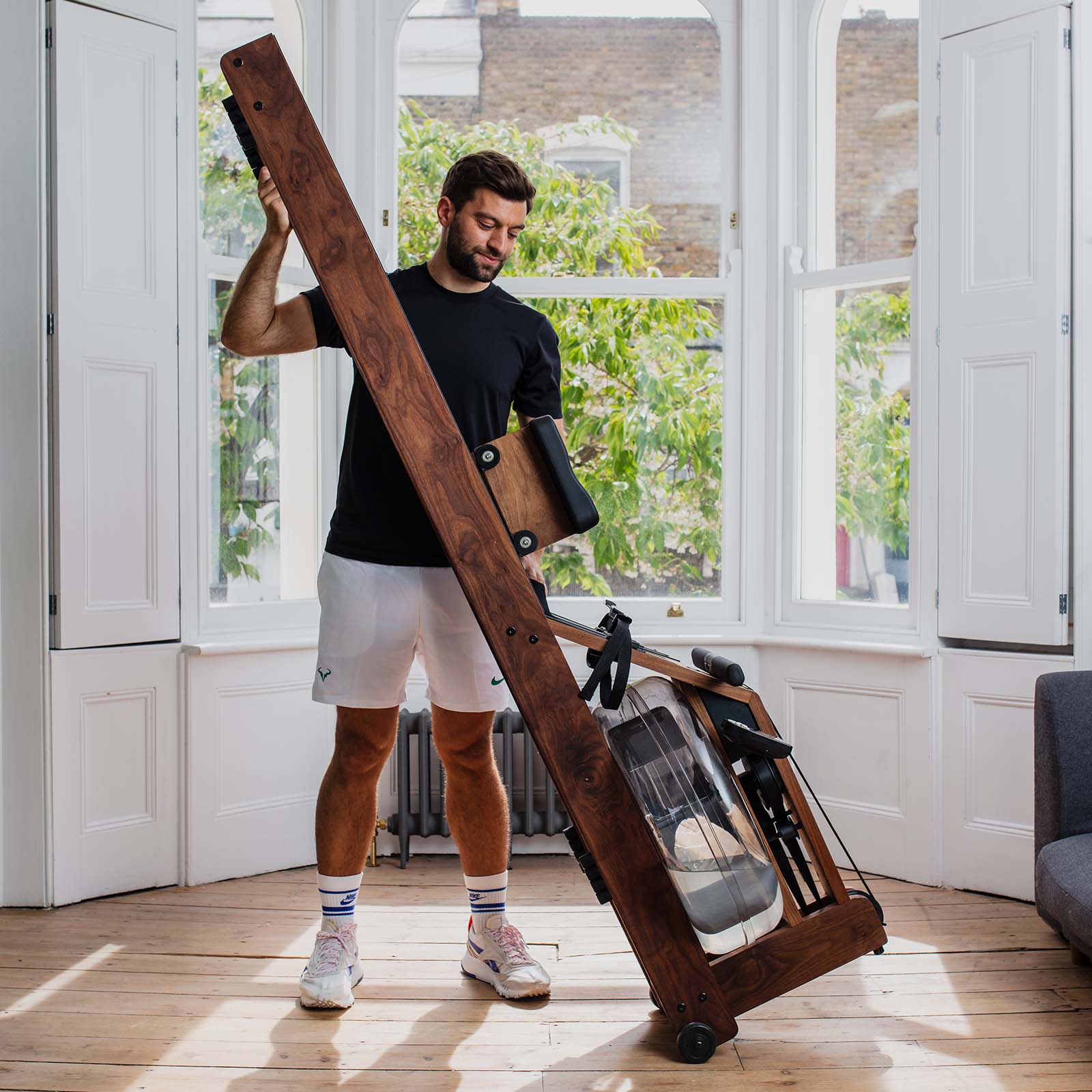 Mann stellt einen WaterRower aus Holz mithilfe der Transportrollen aufrecht auf